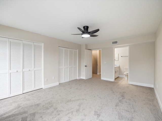 unfurnished bedroom featuring two closets, connected bathroom, light colored carpet, and ceiling fan