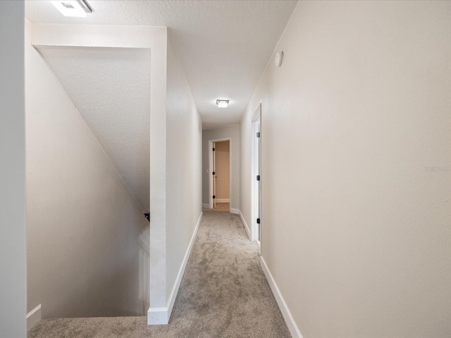 hall with light colored carpet and a textured ceiling