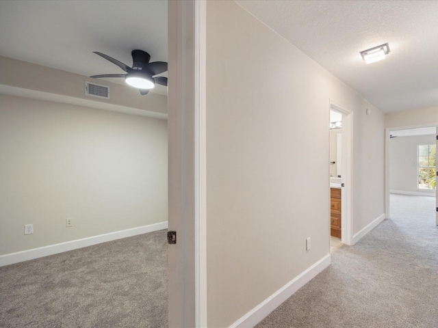 hallway featuring light colored carpet and a textured ceiling