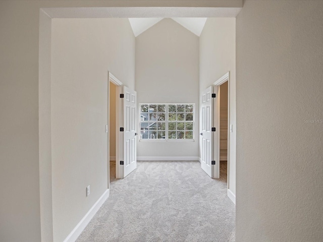 hallway with high vaulted ceiling and light colored carpet