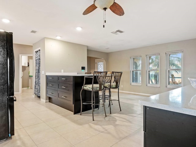 kitchen featuring ceiling fan, black refrigerator, a kitchen breakfast bar, and light tile patterned floors