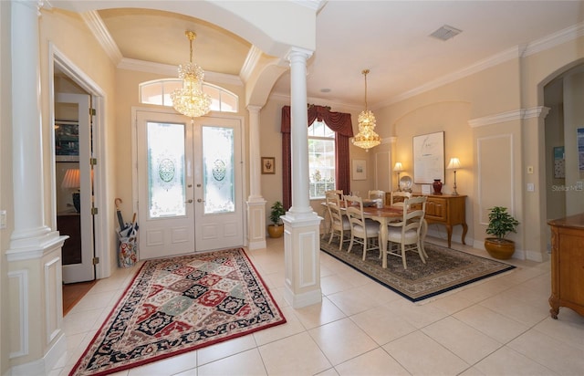 foyer entrance featuring decorative columns, light tile patterned floors, crown molding, and a notable chandelier