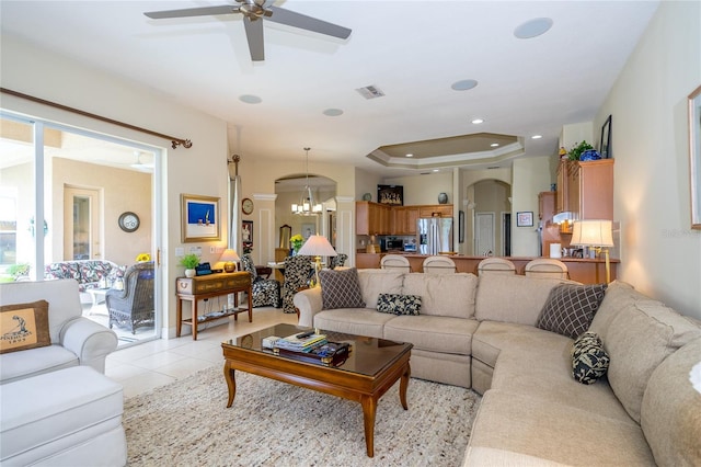 tiled living room featuring a raised ceiling and ceiling fan with notable chandelier