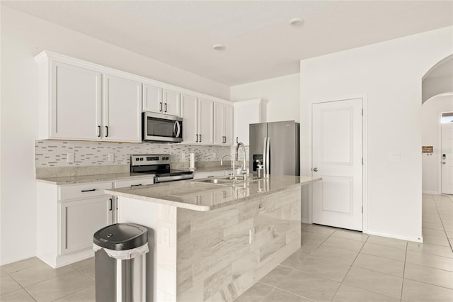 kitchen with appliances with stainless steel finishes, sink, white cabinetry, light tile patterned flooring, and an island with sink