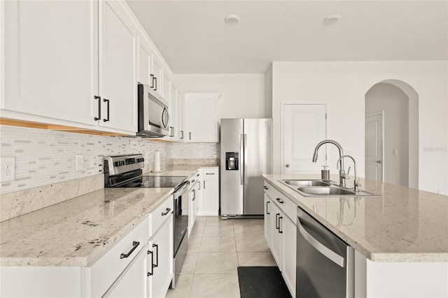 kitchen with appliances with stainless steel finishes, sink, white cabinetry, light tile patterned floors, and a kitchen island with sink