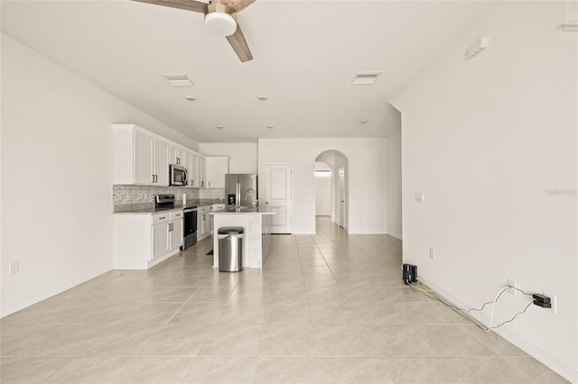 kitchen with ceiling fan, appliances with stainless steel finishes, white cabinetry, an island with sink, and decorative backsplash