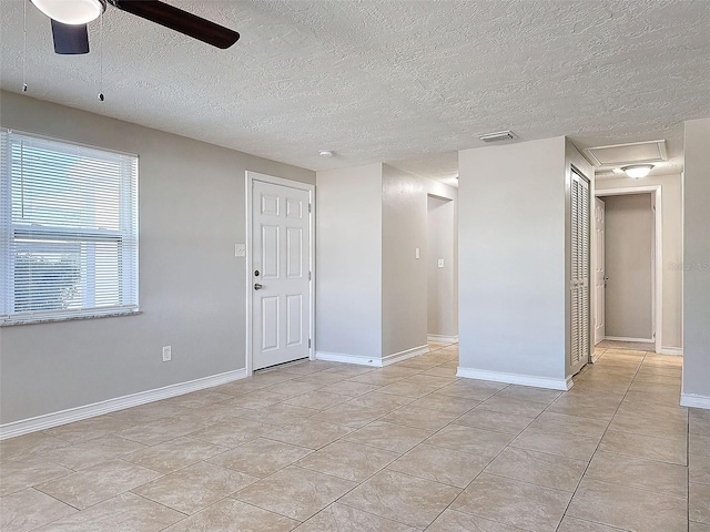 empty room with ceiling fan, light tile patterned floors, and a textured ceiling