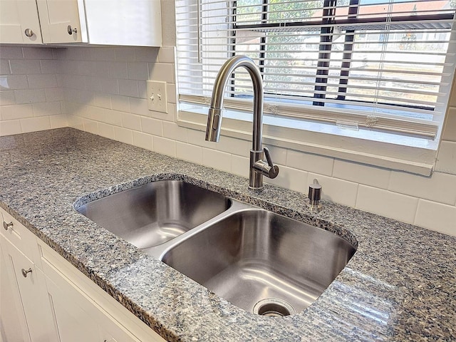 interior details with white cabinets, decorative backsplash, dark stone counters, and sink