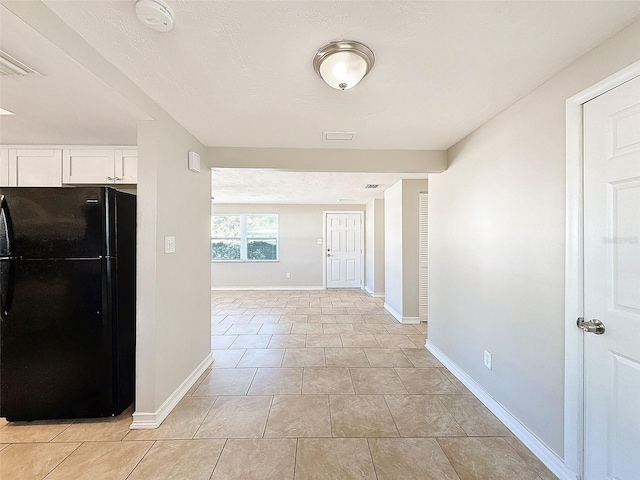 interior space with light tile patterned floors, black refrigerator, and white cabinets