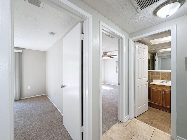 corridor featuring sink, a textured ceiling, and light tile patterned flooring