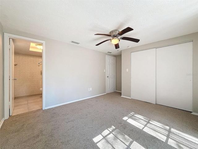 unfurnished bedroom featuring a textured ceiling, a closet, carpet flooring, ceiling fan, and ensuite bathroom