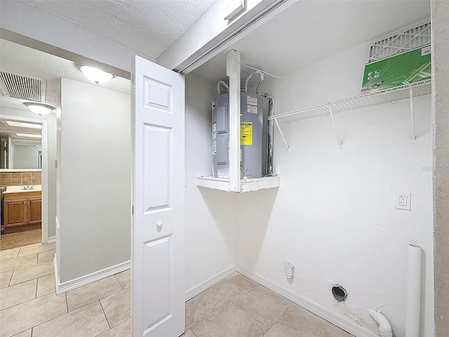 laundry area featuring water heater, light tile patterned flooring, and a textured ceiling