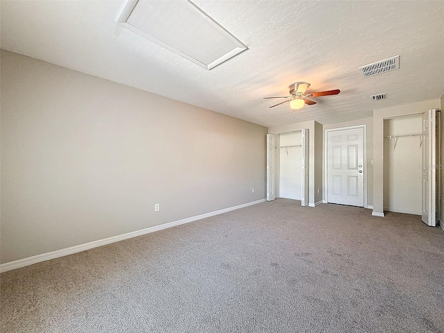 unfurnished bedroom featuring ceiling fan, multiple closets, carpet, and a textured ceiling