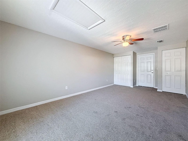 unfurnished bedroom featuring ceiling fan, a textured ceiling, multiple closets, and dark colored carpet