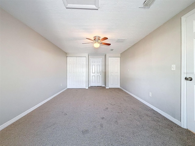 unfurnished bedroom featuring a textured ceiling, ceiling fan, carpet, and multiple closets