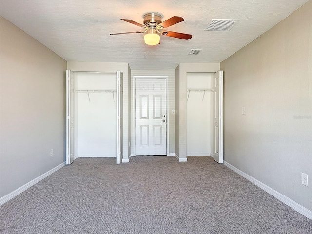 unfurnished bedroom with light carpet, ceiling fan, a textured ceiling, and two closets