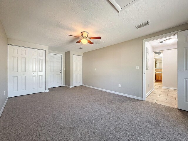 unfurnished bedroom with ceiling fan, a textured ceiling, light carpet, and multiple closets