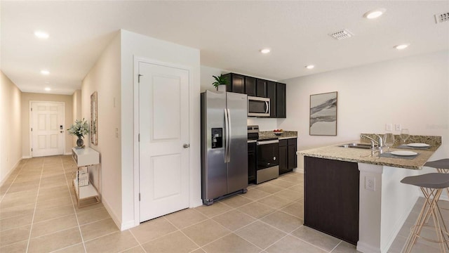 kitchen featuring sink, light tile patterned floors, appliances with stainless steel finishes, a kitchen bar, and kitchen peninsula