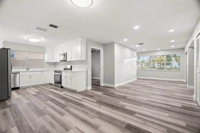 kitchen with stainless steel appliances, sink, white cabinets, and light wood-type flooring