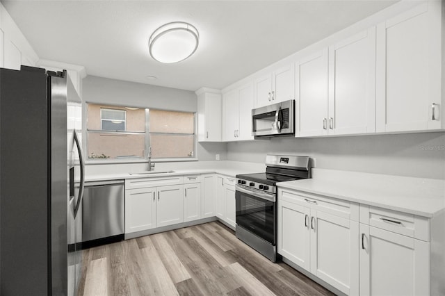 kitchen with stainless steel appliances, sink, white cabinets, and light hardwood / wood-style floors