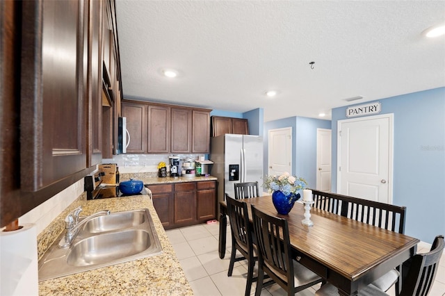 kitchen featuring light stone countertops, stainless steel appliances, sink, backsplash, and light tile patterned floors