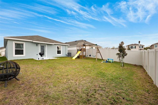 back of house featuring a playground, a yard, central AC, and a fire pit