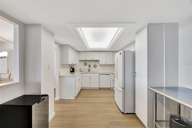 kitchen with light countertops, freestanding refrigerator, white cabinets, a sink, and dishwasher