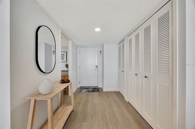 corridor featuring baseboards, a textured ceiling, and light wood finished floors