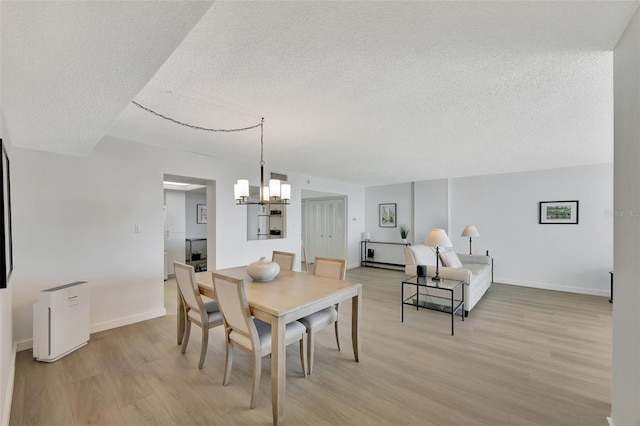 dining room with a chandelier, a textured ceiling, light wood-type flooring, and baseboards