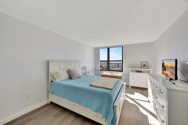 bedroom featuring light wood-style floors, a textured ceiling, and baseboards