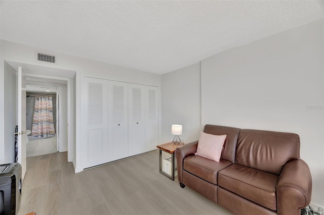 living area with light wood-style flooring, visible vents, and a textured ceiling