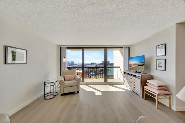 sitting room featuring light wood finished floors, a wall of windows, and baseboards