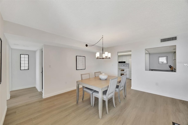 dining room featuring light wood-style floors, visible vents, a textured ceiling, and baseboards