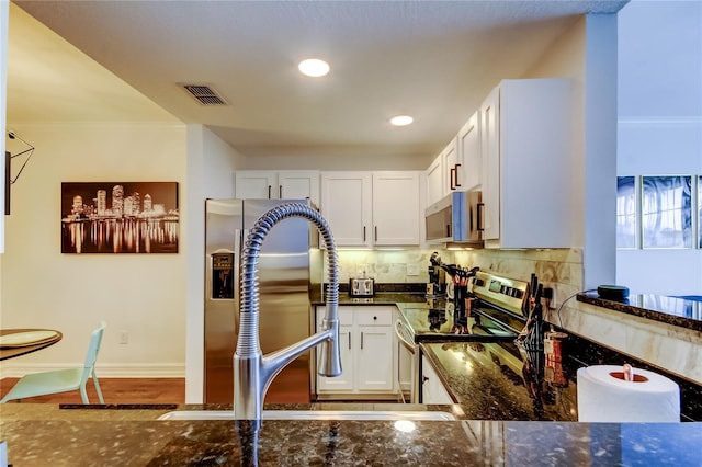 kitchen featuring crown molding, appliances with stainless steel finishes, dark stone countertops, white cabinets, and decorative backsplash