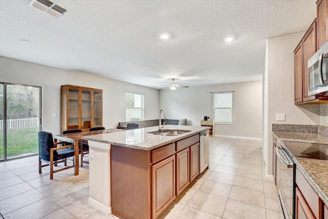 kitchen with sink, light stone counters, a center island with sink, light tile patterned floors, and appliances with stainless steel finishes