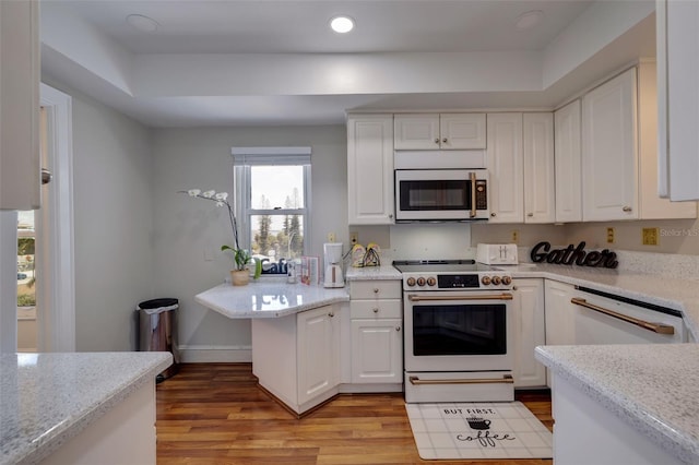 kitchen with white appliances, white cabinetry, light wood-type flooring, and light stone counters