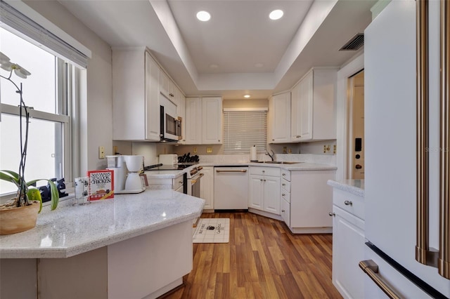 kitchen with light hardwood / wood-style flooring, a raised ceiling, white cabinets, light stone counters, and white appliances