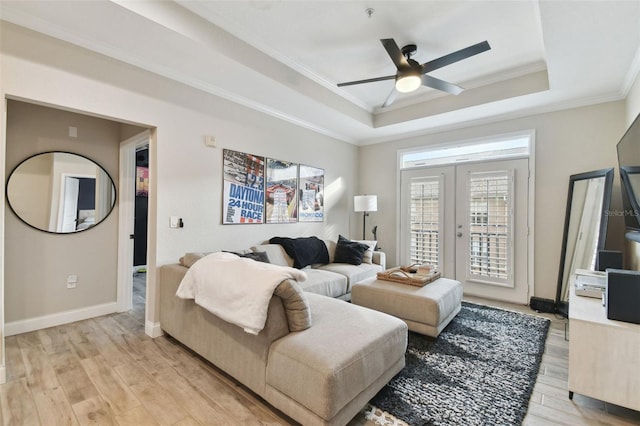 living room featuring french doors, ornamental molding, light wood-type flooring, ceiling fan, and a tray ceiling