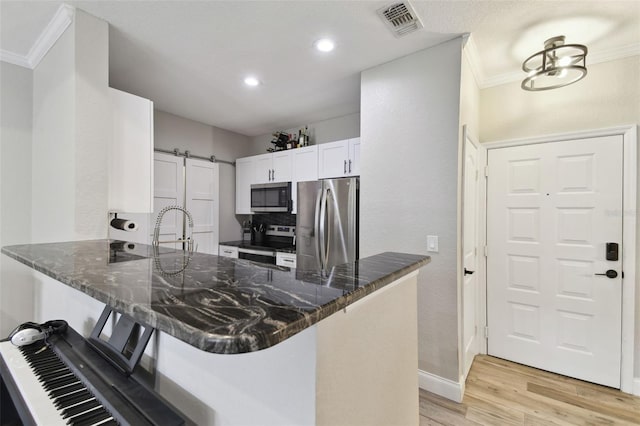 kitchen featuring appliances with stainless steel finishes, white cabinetry, dark stone countertops, kitchen peninsula, and a barn door