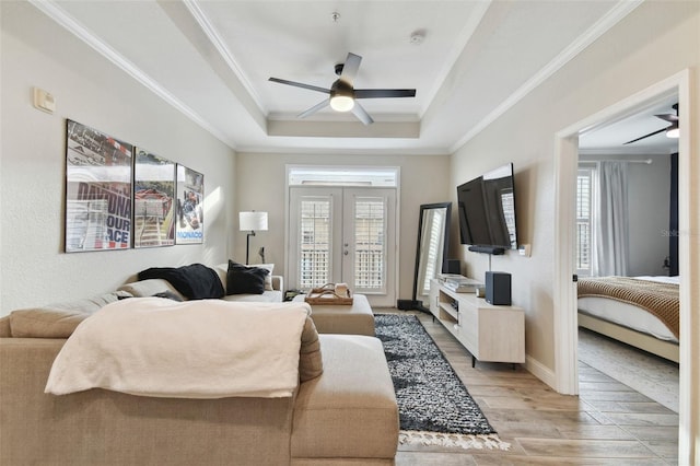 living room with light wood-type flooring, french doors, plenty of natural light, and a tray ceiling