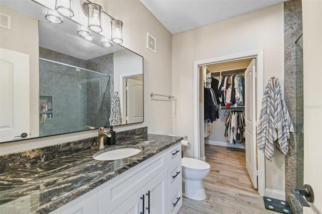 bathroom with wood-type flooring, toilet, vanity, and a tile shower