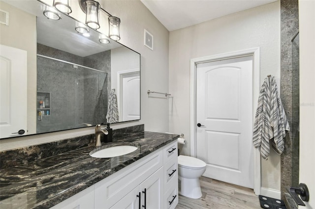 bathroom featuring vanity, toilet, a tile shower, and wood-type flooring