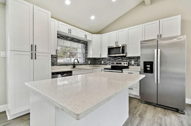 kitchen featuring appliances with stainless steel finishes, lofted ceiling, white cabinetry, and a center island