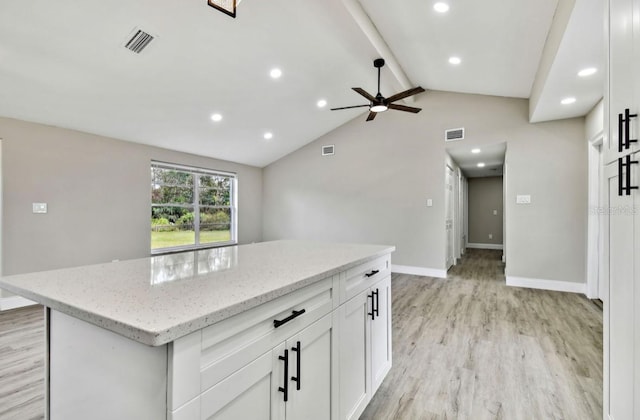 kitchen with a center island, white cabinetry, lofted ceiling with beams, light wood-type flooring, and light stone counters