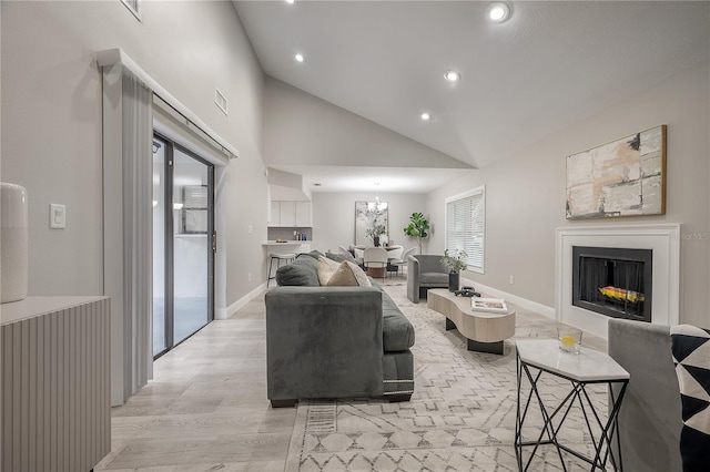 living room with high vaulted ceiling, an inviting chandelier, and light wood-type flooring