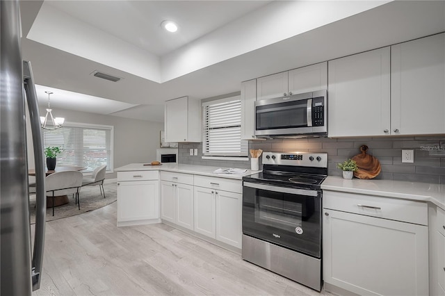 kitchen with white cabinets, stainless steel appliances, light wood-type flooring, and backsplash