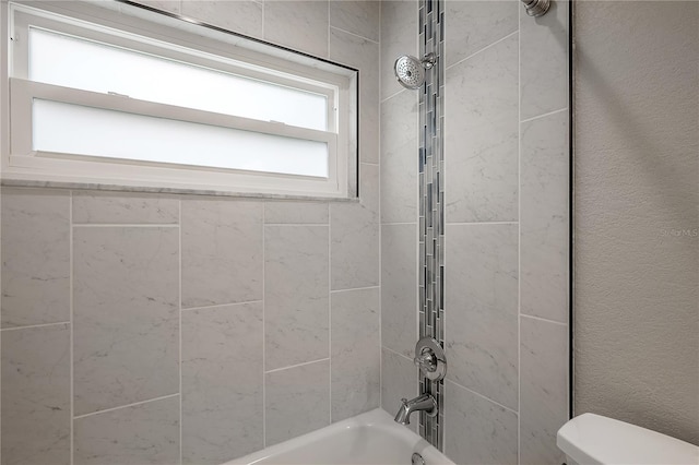 bathroom featuring tiled shower / bath combo and toilet