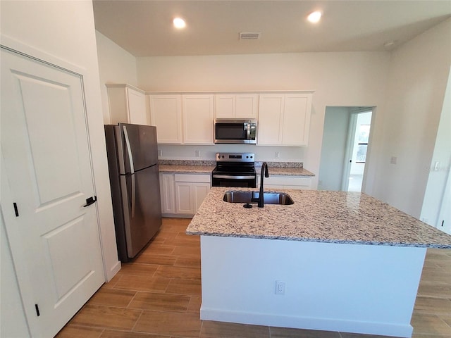 kitchen featuring sink, white cabinetry, appliances with stainless steel finishes, light stone countertops, and a kitchen island with sink