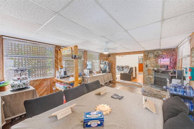 dining area with ceiling fan, a paneled ceiling, and wood walls