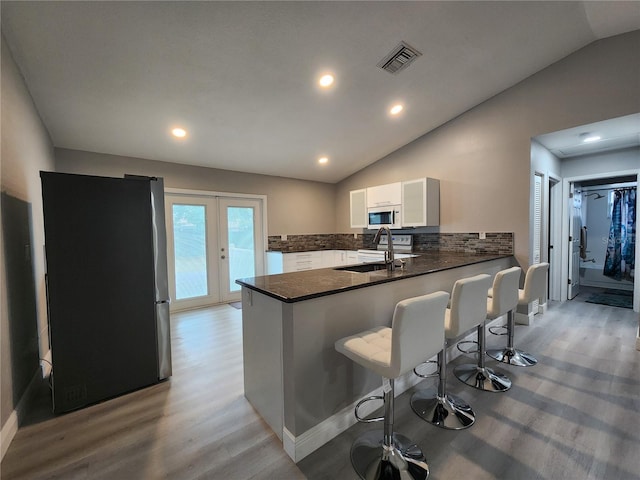 kitchen with white cabinetry, tasteful backsplash, stainless steel fridge, kitchen peninsula, and vaulted ceiling